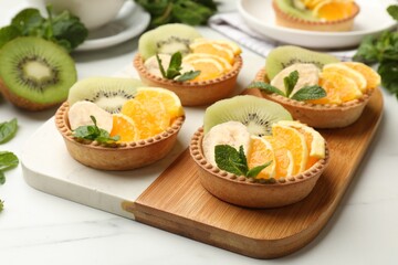 Tartlets with fruits and mint on white table, closeup. Delicious dessert