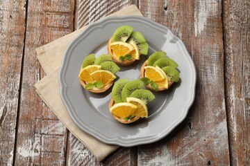 Tartlets with fruits and mint on wooden table, top view. Delicious dessert