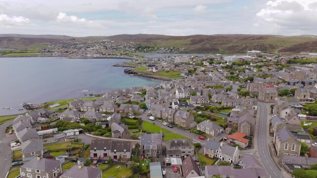 An aerial shot of Lerwick, Shetland in Scotland, sweeping over the town, with hills and beaches in the background.