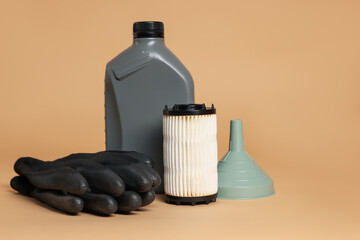 Motor oil in plastic canister, filter, gloves and funnel on beige background