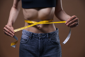 Anorexic woman measuring her waist on brown background, closeup
