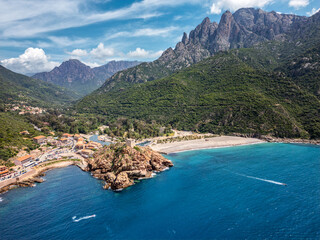 Aerial view of the Genoise tower on a rocky outcrop and the beach at Porto on the west coast of the Mediterranean island of Corsica with mountains behind