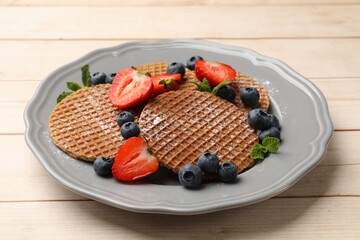 Tasty Dutch waffles (stroopwafels), mint and berries on light wooden table, closeup