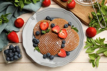 Tasty Dutch waffles (stroopwafels), mint and berries on light wooden table, flat lay