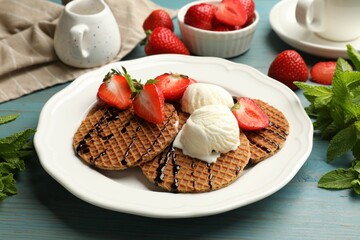 Tasty Dutch waffles (stroopwafels) with ice cream, chocolate sauce, mint and strawberries on light blue wooden table, closeup