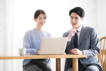 逆光のオフィスでパソコンを見るスーツを着たビジネスマン男女　新人指導やコミュニケーションなどのイメージ