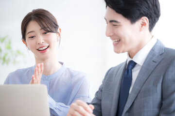 逆光のオフィスでパソコンを見るスーツを着たビジネスマン男女　新人指導やコミュニケーションなどのイメージのクローズアップ