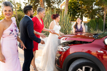 Bride, groom, and guests inspecting broken down car on wedding day