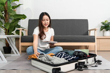 Travel Preparation. A woman sits on the floor, reviewing her packing list while organizing her suitcase.