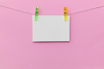 Blank card suspended on a string with colorful clips against a pink background creating a bright and cheerful display