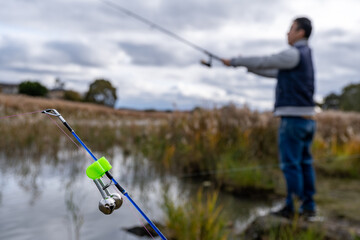 A fishing bite alarm bell clipped onto a rod, with an Asian man casting his fishing line in the...