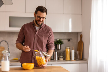 Man is preparing cereal for breakfast, pouring milk over a bowl of cereal in a cozy kitchen....