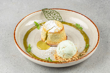 A golden matcha lava cake with powdered sugar and green tea sauce served alongside a scoop of mint ice cream and crumbled nuts, elegantly garnished with fresh mint.