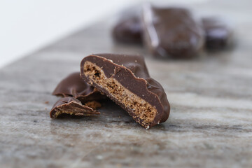 Decadent Chocolate Covered Biscuit Piece, broken in half to clearly show its textured, crumbly interior with hick layer of chocolate coating isolated on marble side view of sweet treat