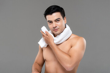 Shirtless man drying face with white towel after workout on gray background, men skin care and beauty concept