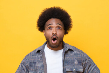 Surprised man looking up and reacts with shock on yellow background