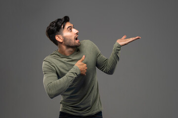 Surprised shocked man pointing and presenting with open hand against isolated gray background studio shot