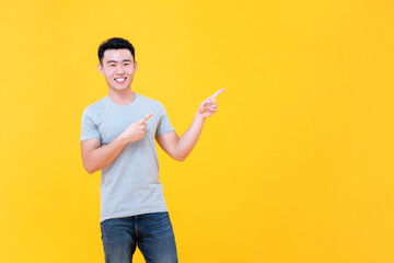 Smiling Asian man in casual outfit pointing hands to copy space on yellow background with cheerful expression