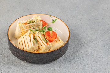 Grilled tortilla wraps filled with fresh vegetables and herbs served in a modern bowl with cherry...