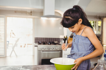 Child whisking batter in green and white bowl on tiled kitchen countertop near stove, copy space