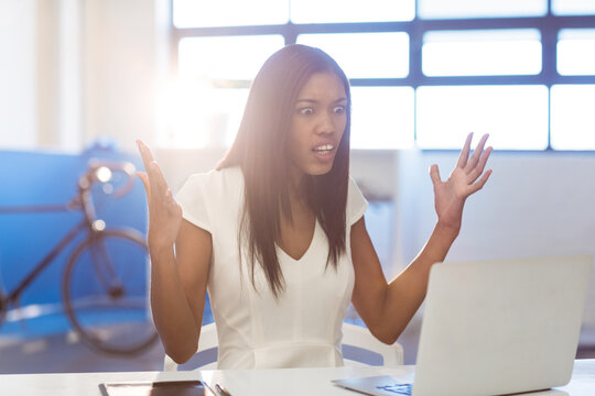 African American woman raising hands and looking at laptop on desk at modern office with bicycle