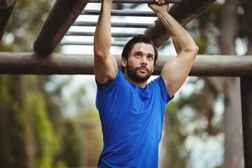 Man hanging from rust-colored horizontal bars in park fitness area under soft natural light