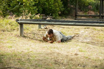 Male soldier wearing camouflage uniform crawling under netted metal beam on obstacle course