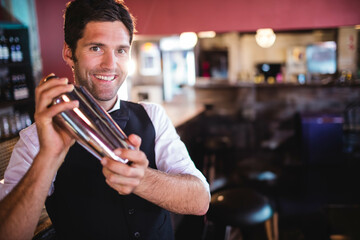 White mid adult male bartender shaking stainless steel cocktail shaker behind wooden bar counter