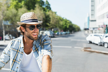 Male cyclist wearing straw fedora and sunglasses riding bicycle along urban street, copy space