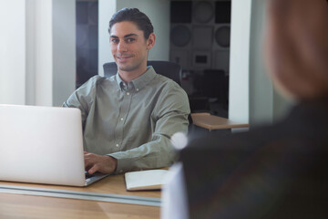 Man typing on laptop wearing gray-green shirt glancing at colleague in office area copy space