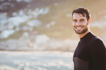 Adult man standing on sandy shore wearing wetsuit smiling at camera under golden light, copy space