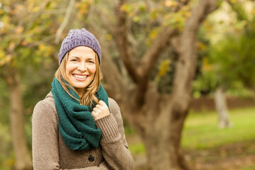 Woman standing in park in autumn wearing purple beanie green scarf and brown cardigan, copy space