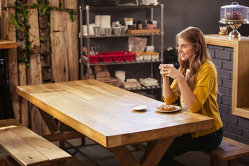 White coffee cup and pastry on plate resting at light-wood communal table in rustic industrial café