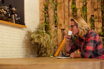 Small white espresso cup steaming on large wooden table in cafe with hanging green plants