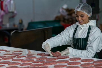Female processing operator arranging burger patties on stainless steel table in plant, copy space