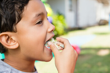Biting into frosted cupcake with sprinkles while standing in front yard by white house, copy space