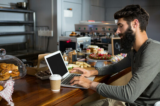Naklejki Laptop sitting open beside steaming paper coffee cup on wooden counter under glass pastry domes