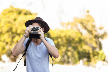 Man holding vintage instant camera, capturing sunlit tree canopy in green park in bright sunlight