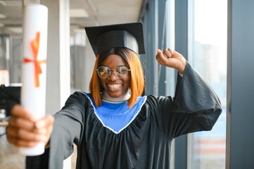 Portrait of African American graduate student in toga holding her diploma