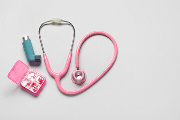 Composition with asthma inhaler, stethoscope and box of pills on grey background