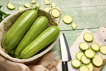 Board and wicker basket with fresh zucchini on green wooden background