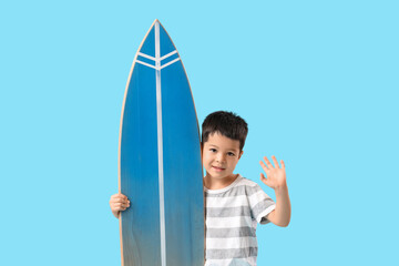 Cute little Asian boy with surfboard on blue background