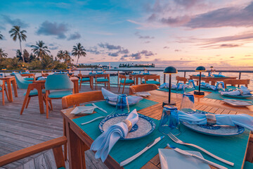 Fototapeta premium Outstanding overwater restaurant with dinner tables set for romantic luxury dining under amazing gorgeous sunset sky with clouds candles creating intimate mood tropical resort elegant evening scene