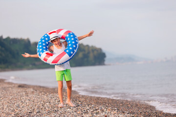 Child enjoying playing on beach with inflatable ring in american flag colors on sunny day