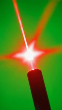 A red laser beam emits from a black device against a bright green background. The scene is isolated, highlighting the contrast between the colors.