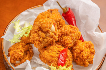 Crispy golden fried chicken bites served hot with red chili peppers and garnished with fresh frisee...