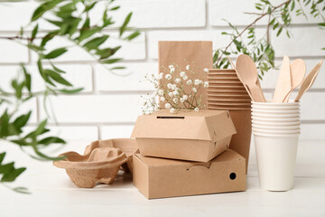 Eco tableware with plant branches on white wooden table near brick wall