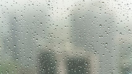 Close-up view of raindrops on a glass window during a rainy day, with a soft, blurry background creating a calm and moody atmosphere.