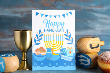 Hanukkah composition with greeting card and traditional decorations on blue wooden background