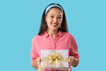 Beautiful young Asian woman with gift box on blue background